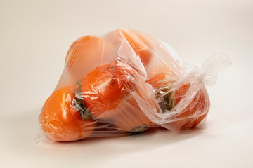 Ripe juicy orange persimmon in a plastic transparent bag beige background. Selective focus.