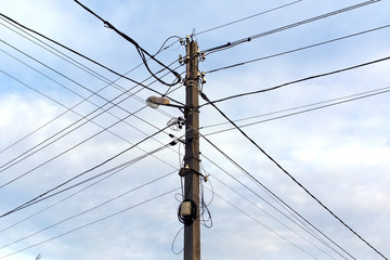 Electric pole with a lantern and electric wires. Light blue sky on background.