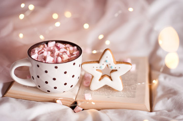 Cup of coffee with gingerbread staying on open book closeup over glowing lights closeup. Good morning. Xmas. Winter holiday season.