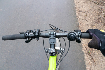Cyclist on the bike path. First person view. Focus on the hand and the handlebars. It's cold, man in cycling clothes. On the track leaves and branches. Bike controls closeup.