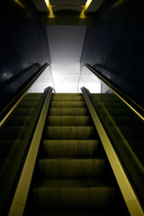 Escalator with recessed footlights glowing in darkness.  Abstract transportation and architecture photo. Public interior of modern multistory building or subway station. Moving staircase in backlight.