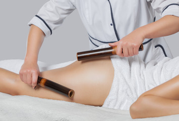 Masseur makes anti-cellulite massage with bamboo sticks on thighs, legs and buttocks in a beauty salon. Cellulite and Overweight Treatment.