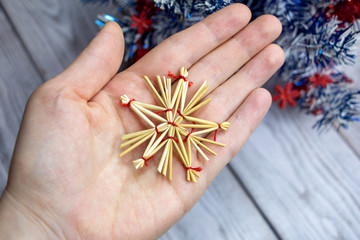 A star made of straw and red threads on an open palm..Homemade Christmas toy from natural materials.
