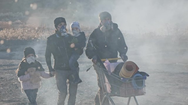 Survivor family in gas mask going through clouds of toxic smoke and cinder in desolate and burned out forest landscape.