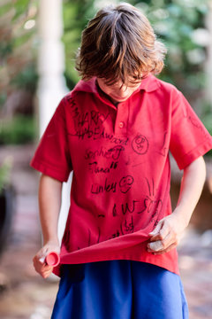 Small boy wearing a school shirt covered in signatures