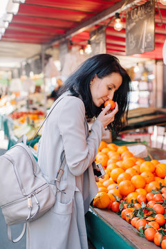 Brunette woman smelling orange at street market