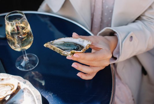 Crop hand holding oyster and glass of white wine
