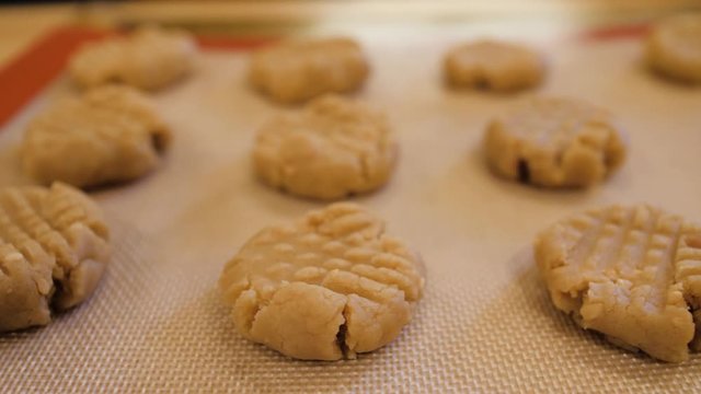 Panning over a tray of uncooked peanut butter cookies. Homemade cookie dough on cookie sheet with silicone baking mat.