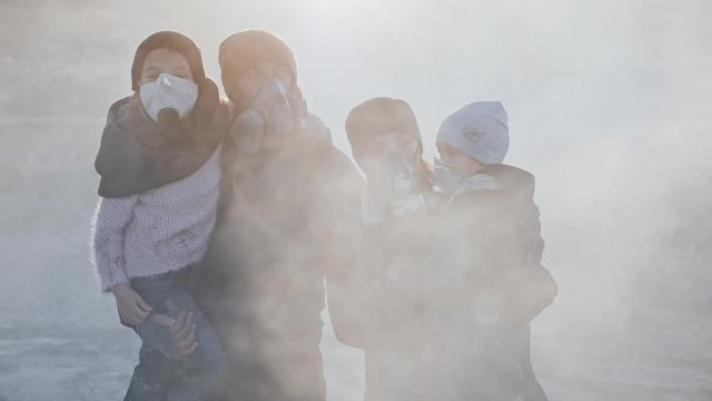 Portrait Of Survivor Family In Gas Mask Standing In Clouds Of Toxic Smoke And Cinder In Empty Dead Landscape.