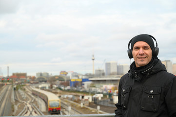Smiling man listens to music. In the background it can be seen the city of Berlin (Germany) from the Warschauer Strasse in winter time