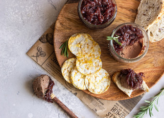 Fresh homemade chicken liver pate and onion chutney (marmalade) in a jar, bread and crackers on a wooden plate. Light grey background, selective focus.