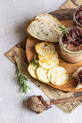 Fresh homemade chicken liver pate and onion chutney (marmalade) in a jar, bread and crackers on a wooden plate. Light grey background, selective focus.