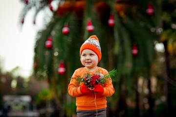 a small, beautiful girl in bright clothes,and in an orange hat, dancing near a Christmas tree, with a Christmas bouquet in her hand