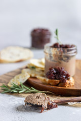Fresh homemade chicken liver pate and onion chutney (marmalade) in a jar, bread and crackers on a wooden plate. Light grey background, selective focus.