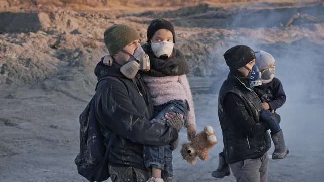 Survivor family in gas mask going through clouds of toxic smoke and cinder in desolate and burned out forest landscape.