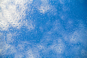 blue water drops background on glass amid blue sky with white clouds