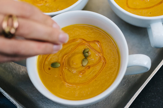Woman adding pepitas to butternut squash soup