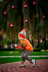 a small, beautiful girl in bright clothes,and in an orange hat, dancing near a Christmas tree, with a Christmas bouquet in her hand