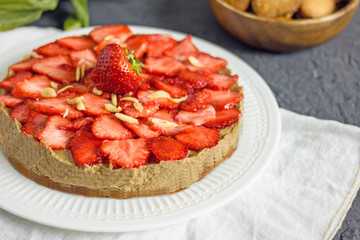 Vegan Strawberry Cake. Homemade cake with raw cream of dates and coconut milk, without eggs and gluten on almond flour on a white plate on a dark table. The concept of proper nutrition, sweets without
