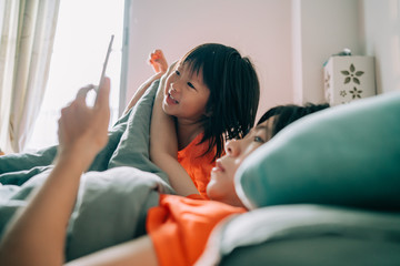 Little girl and mom watching videos on the bed with cell phone
