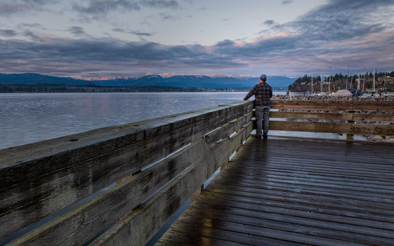 Man standing on a pier looking at mountains across a beautiful sea