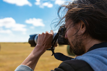 Young male photographer with long hair shooting the horizon with a professional DSLR camera and a long telephoto lens during countryside shooting