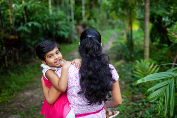 Young woman walking on a village path carrying her little daughter on her lap