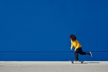 Ethnic skater riding alongside blue wall