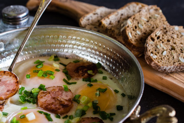 fried eggs with sausages in a copper frying pan
