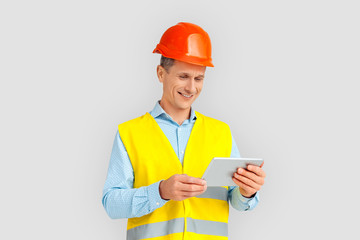 Construction. Mature man in hardhat and uniform standing isolated on white watching video on digital tablet smiling cheerful