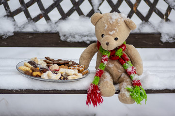 Beige plushy teddy bear with red green striped knitted scarf sitting with Christmas cookies on the...