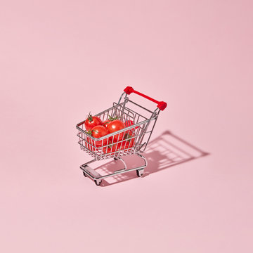Ripe tomatoes in a shopping cart presented on a pink background with space for text. Shopping concept