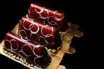 Three chocolate desserts with chocolate mirror glaze peanuts and silver circles decoration
