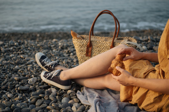 Crop woman eating croissant on beach