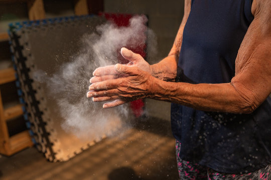 An anonymous fit woman in her seventies claps chalk off of her hands while working out at a gym.