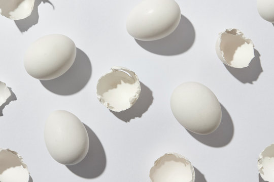 Pattern of white eggs and eggshell on a gray background with shadows. Flat lay