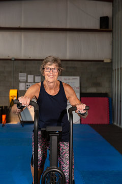 Portrait of a fit woman in her seventies smiling and exercising on a stationary bike in a gym.