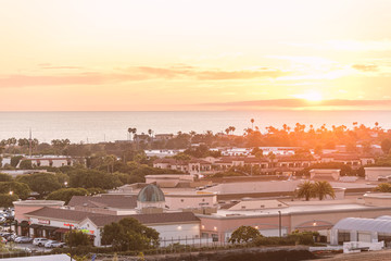 Sunset over a small town on the pacific coast with buildings, trees and ocean under a bright yellow sunset.