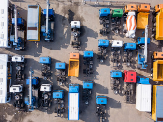 Construction machines empty dump trucks, cement mixers, tow trucks with hard shadows on a parking. Aerial top view from drone.
