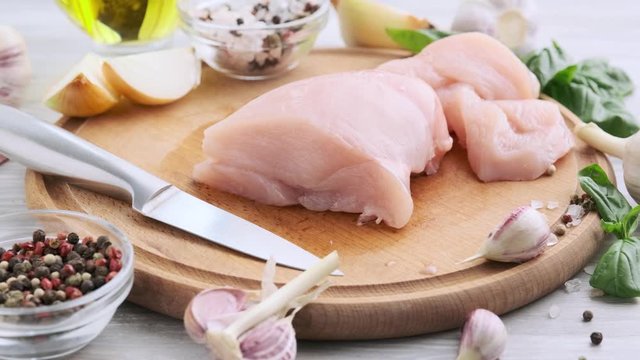 Fresh raw chicken meat with basil and garlic on a wooden board with a stainless steel knife. Slow motion. 4k