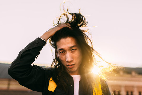 Attractive chinese man waving is long hair at sunset