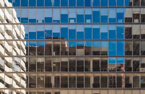 Fachada de un edificio acristalado donde se reflejan el resto de edificios