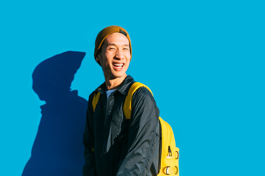 Portrait of stylish young chinese man posing in front of a blue wall and smiling