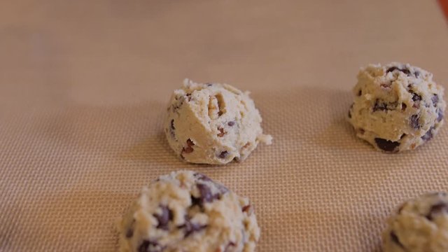 Placing chocolate chip cookie dough balls on cookie sheet. Scooping raw cookie dough onto silicone baking mat.