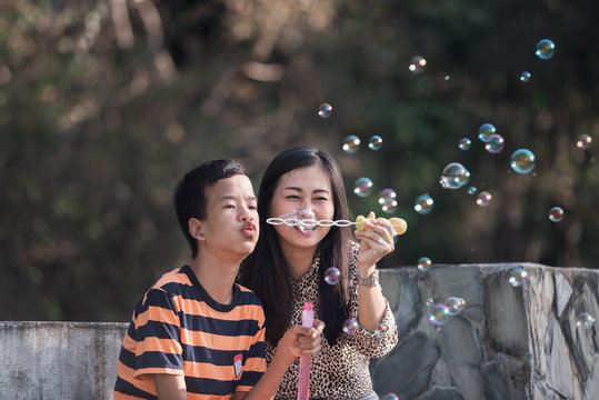 Happy Asian boy with Down's syndrome and mother Blowing bubbles in the park