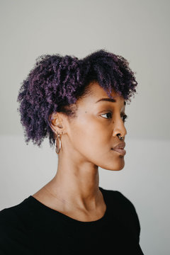 A beautiful african american woman with purple hair against a white wall