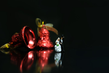 Miniature wedding concept - bride and groom walking on shiny floor with bell ornament