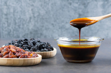 grape molasses in glass bowl , in wooden spoon and dried black and green grapes on rustic...