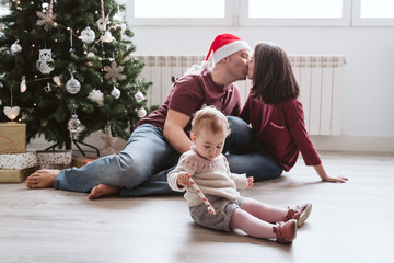 Happy family with baby girl at home by the Christmas tree