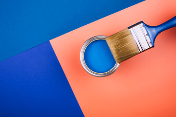 Brush on open can of blue paint on coral and blue background. Concept of changing color of the year.